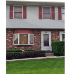 Exterior of townhouse with brick first floor and light gray siding with red shutters on the second floor