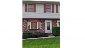 Exterior of townhouse with brick first floor and light gray siding with red shutters on the second floor