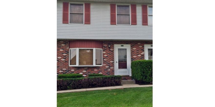 Exterior of townhouse with brick first floor and light gray siding with red shutters on the second floor