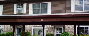 Exterior of townhouse with light brown brick on the first floor, brown siding with white shutters on the second floor and carport out front