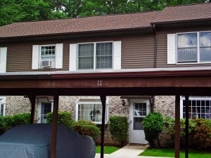 Exterior of townhouse with light brown brick on the first floor, brown siding with white shutters on the second floor and carport out front