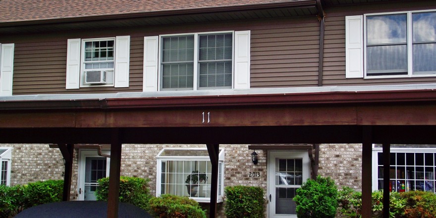 Exterior of townhouse with light brown brick on the first floor, brown siding with white shutters on the second floor and carport out front