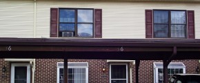 Exterior of townhouse with brick first floor and yellow siding with maroon shutters on the second floor with carport out front