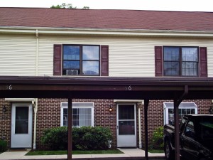 Exterior of townhouse with brick first floor and yellow siding with maroon shutters on the second floor with carport out front