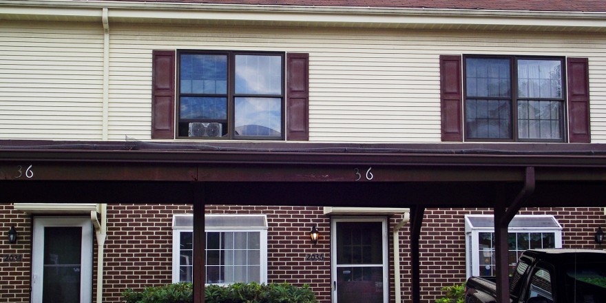 Exterior of townhouse with brick first floor and yellow siding with maroon shutters on the second floor with carport out front