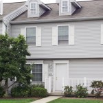 Exterior of townhome with light gray siding and white shutters, door, and trim