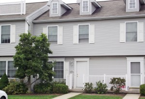 Exterior of townhome with light gray siding and white shutters, door, and trim