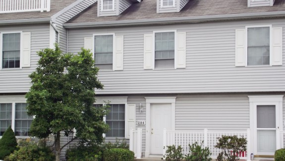 Exterior of townhome with light gray siding and white shutters, door, and trim