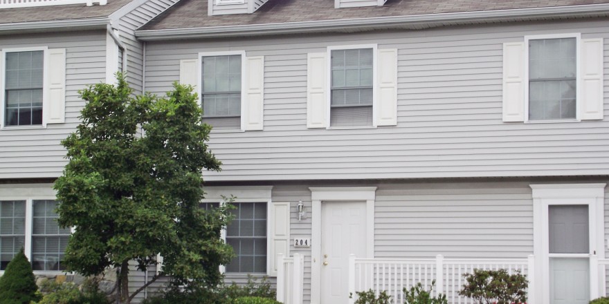 Exterior of townhome with light gray siding and white shutters, door, and trim