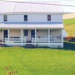 Exterior of duplex with large front yard, covered front porch, and siding with a metal roof