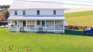 Exterior of duplex with large front yard, covered front porch, and siding with a metal roof