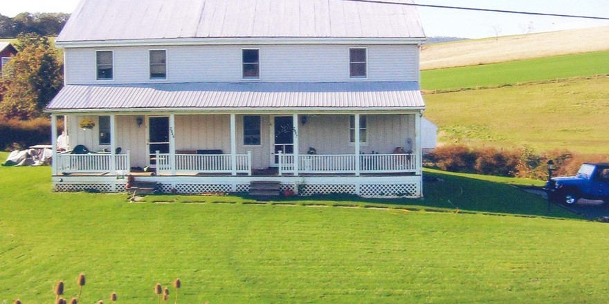 Exterior of duplex with large front yard, covered front porch, and siding with a metal roof