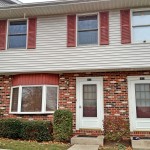 Exterior of townhouse with brick first floor and light gray siding with red shutters on the second floor