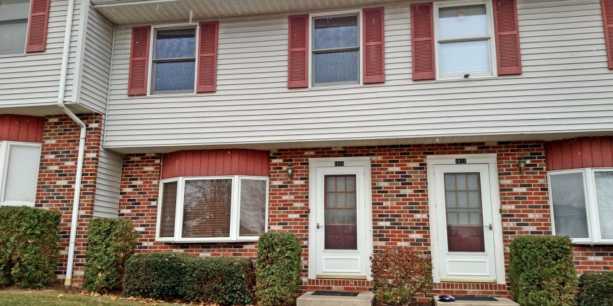 Exterior of townhouse with brick first floor and light gray siding with red shutters on the second floor