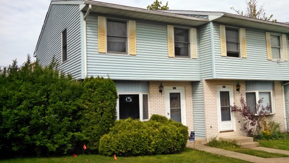 Exterior of townhouse with yellow brick and blue siding with yellow shutters