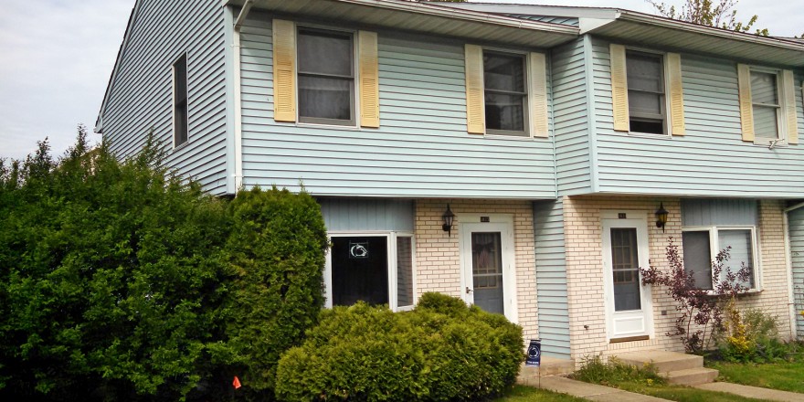 Exterior of townhouse with yellow brick and blue siding with yellow shutters
