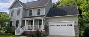 Exterior of two story house with covered front porch, garage, siding, stone, and landscaping.