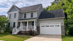 Exterior of two story house with covered front porch, garage, siding, stone, and landscaping.