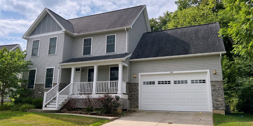 Exterior of two story house with covered front porch, garage, siding, stone, and landscaping.