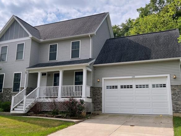 Exterior of two story house with covered front porch, garage, siding, stone, and landscaping.