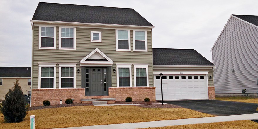 Exterior of house with siding and brick, large garage, driveway, lawn and sidewalk