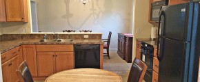 Kitchen with small table, black appliances, wood cabinets, and brown marble-style countertops