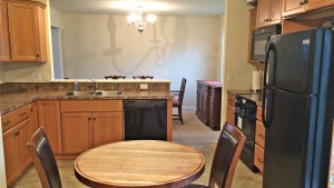 Kitchen with small table, black appliances, wood cabinets, and brown marble-style countertops