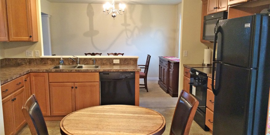 Kitchen with small table, black appliances, wood cabinets, and brown marble-style countertops