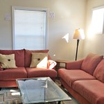 Carpeted living room with red couch and love seat, glass coffee table, accent rug, windows and lamps