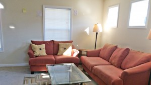 Carpeted living room with red couch and love seat, glass coffee table, accent rug, windows and lamps