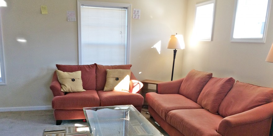 Carpeted living room with red couch and love seat, glass coffee table, accent rug, windows and lamps