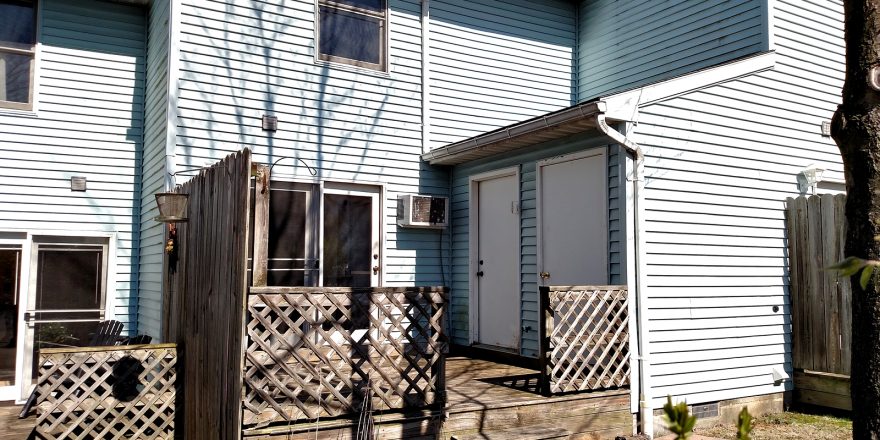 Exterior of townhouse with blue siding and wooden deck off the back of the house