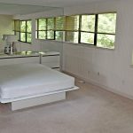 Bedroom with queen bed on modern bedframe, large mirror wall and two large windows