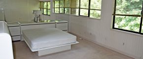 Bedroom with queen bed on modern bedframe, large mirror wall and two large windows