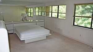 Bedroom with queen bed on modern bedframe, large mirror wall and two large windows