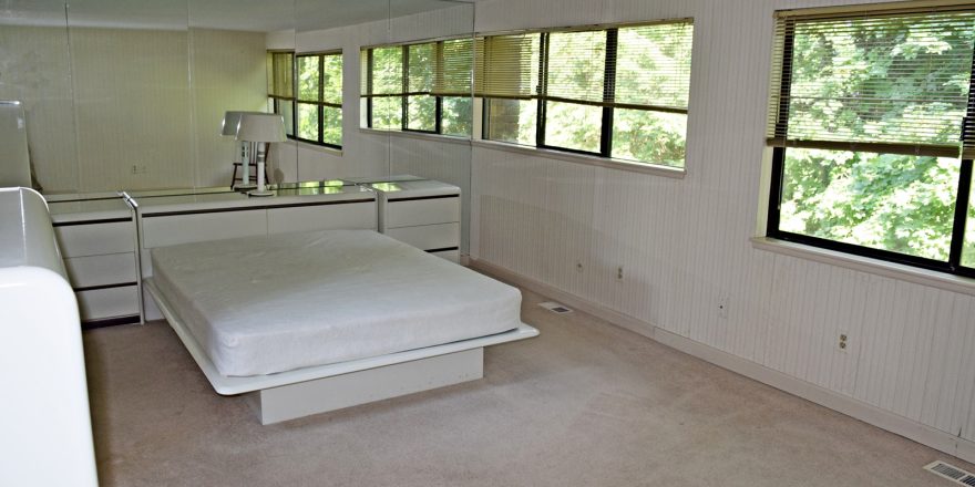 Bedroom with queen bed on modern bedframe, large mirror wall and two large windows