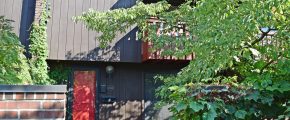 Exterior of a townhome with a bright red front door and brown large-panel siding