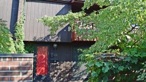 Exterior of a townhome with a bright red front door and brown large-panel siding