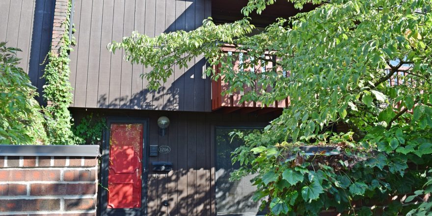 Exterior of a townhome with a bright red front door and brown large-panel siding