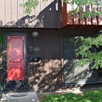Exterior of a townhome with a bright red front door and brown large-panel siding