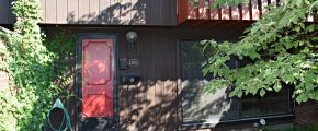 Exterior of a townhome with a bright red front door and brown large-panel siding