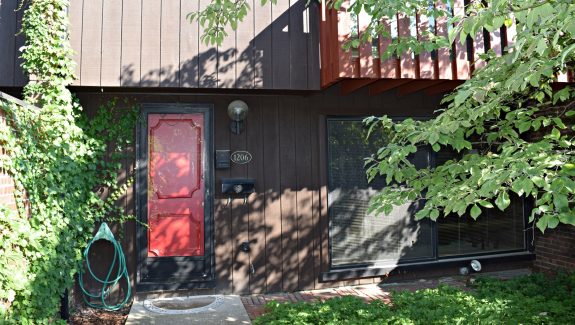 Exterior of a townhome with a bright red front door and brown large-panel siding