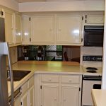 Kitchen with white cabinets, white, black and stainless appliances. There is a small serving window opening to the dining room