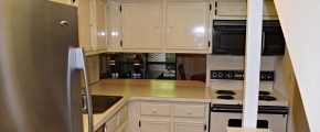 Kitchen with white cabinets, white, black and stainless appliances. There is a small serving window opening to the dining room