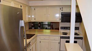 Kitchen with white cabinets, white, black and stainless appliances. There is a small serving window opening to the dining room