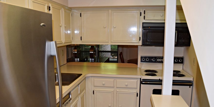 Kitchen with white cabinets, white, black and stainless appliances. There is a small serving window opening to the dining room