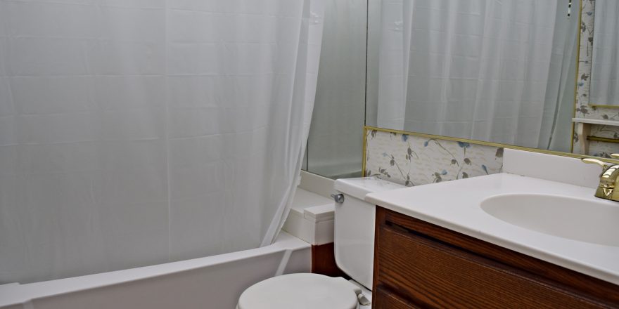 Bathroom with floral wallpaper, shower/tub combo, toilet, and vanity.