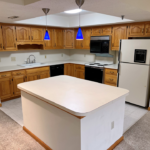 Kitchen with white and black appliances, tile flooring, wood cabinets, and large island