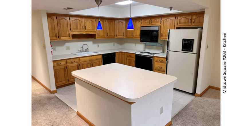 Kitchen with white and black appliances, tile flooring, wood cabinets, and large island