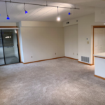 Carpeted living room with arm chair, tv stand, and large windows